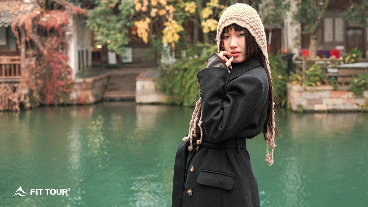 Thiếu nữ mặc áo khoác dài, tạo dáng bên dòng nước trong xanh