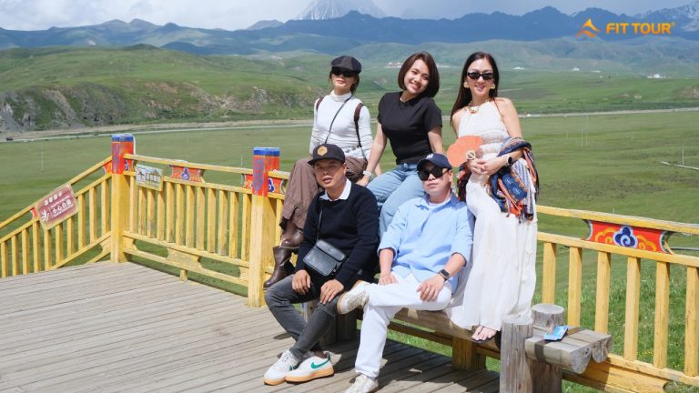 Nhóm du khách FIT TOUR chụp ảnh trên đài quan sát tại Tagong, phía sau là thảo nguyên và núi tuyết