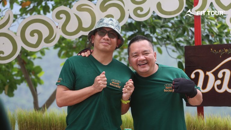 Hai thành viên đoàn motor trip tạo dáng vui vẻ tại điểm dừng chân có bảng hiệu tiếng Thái ở Chiang Mai