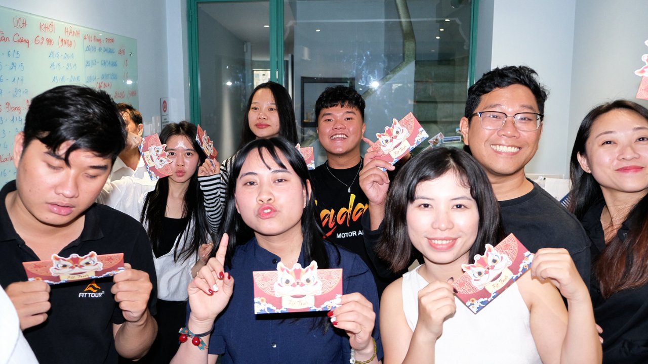 Nhóm nhân viên trẻ trung của FIT Tour tạo dáng vui nhộn, khoe bao lì xì hình lân sư rồng may mắn.